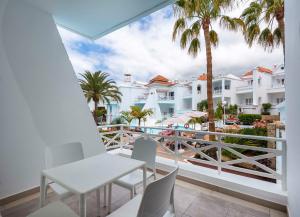 einen Balkon mit einem Tisch, Stühlen und Palmen in der Unterkunft Lagos de Fañabé Beach Resort in Adeje