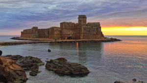 a castle on an island in the water at sunset at Manzoni Apartment in Le Castella