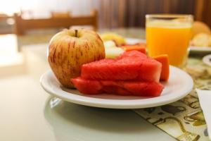 an apple and watermelon on a plate with a glass of orange juice at Sadas Hotel in São Mateus do Sul +6 photos