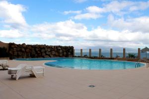 a swimming pool with two chairs and a rock wall at Apartamento Las Rochas in Mindelo