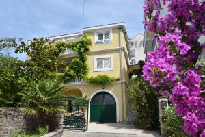 a yellow house with a green door and purple flowers at Huter Apartments in Herceg-Novi