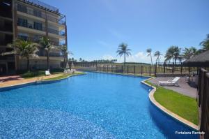 a large blue swimming pool with palm trees and a building at Beach Living Apartamento in Aquiraz