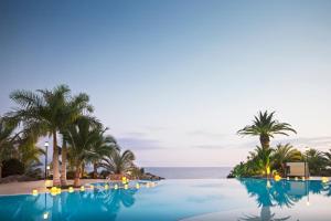 a swimming pool with palm trees and the ocean at Adrián Hoteles Roca Nivaria in Adeje