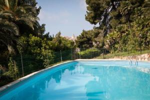 a blue swimming pool with a fence and palm trees at Residence RTA Villa Marina in Imperia