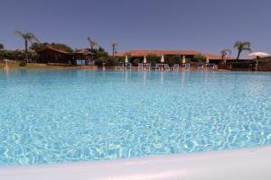 una gran piscina de agua azul con sillas. en Appartamenti residence Vela Blu Golfo Aranci en Marinella