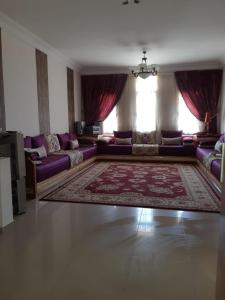 a living room with purple couches and a rug at Résidence al massirra in Fnidek