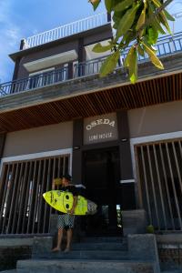 a man holding a yellow surfboard in front of a building at Oseda Nias Surf House in Hilibotodane