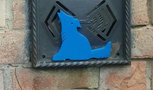 シエナにあるLupo Azzurroの煉瓦壁の金具箱に乗った青い犬