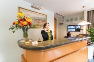 une femme qui parle au téléphone derrière un comptoir avec des fleurs dans l'établissement Hotel Gardenia Sorrento, à Sorrente
