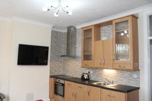 een keuken met houten kasten, een wastafel en een tv bij Van Apartments in Caerphilly