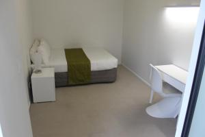 a small white room with a bed and a desk at MCentral Apartments Manukau in Auckland