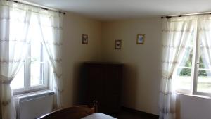 a bedroom with two windows with white curtains at La petite maison normande in Ticheville