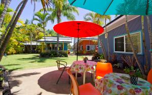 een patio met een tafel en stoelen en een rode parasol bij Bargara Gardens Boutique Villas in Bargara