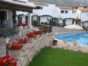 a stone wall next to a swimming pool with flowers at Hotel Resort Nuraghe Arvu in Cala Gonone