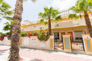 un bâtiment jaune avec des palmiers devant lui dans l'établissement Villa Cabo Roig Coco-Mat, à Playas de Orihuela