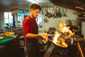 a man cooking food in a pan in a kitchen at Saltmarsh Farmhouse in West Dean