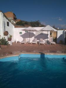 a swimming pool with chairs and umbrellas in front of a house at Casa Rural Tita Sacramento in Hornachos