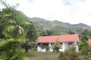 a white building with a red roof with mountains in the background at Daniella's Bungalows in Bel Ombre