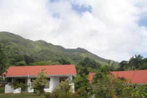 una casa con techo rojo con montañas al fondo en Daniella's Bungalows, en Bel Ombre