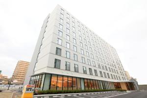 a tall white building with windows on a street at Richmond Hotel Himeji in Himeji