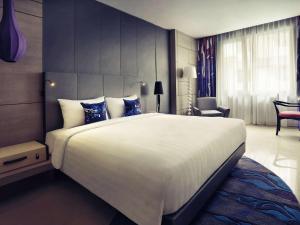 a bedroom with a large white bed with blue pillows at Mercure Jakarta Sabang in Jakarta
