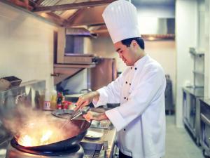 a chef cooking food in a wok in a kitchen at Mercure Jakarta Sabang in Jakarta