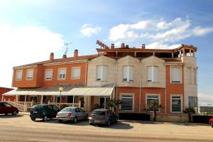 un grande edificio in mattoni con auto parcheggiate in un parcheggio di Hostal Castilla a Benavente