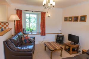 a living room with a leather couch and a television at Ballat Smithy Cottage in Drymen