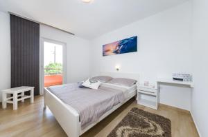 a white bedroom with a bed and a desk at Apartments Orkula in Maslenica