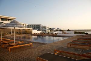 a pool with chairs and umbrellas next to a resort at Memmo Baleeira - Design Hotels in Sagres