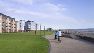 two people riding bikes down a sidewalk next to the beach at Beach Front Ground Floor Apartment in Llanelli +4 photos