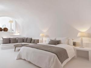 a white bedroom with a large bed and a couch at Katikies Chromata Santorini - The Leading Hotels of the World in Imerovigli