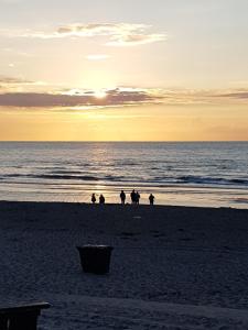 B&B Duinroos De Koog - Texel في دي كوخ: مجموعة من الناس يمشون على الشاطئ عند غروب الشمس