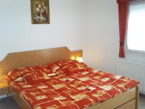 a bedroom with a bed with a red comforter and a window at Andrea Apartmanok in Zalakaros