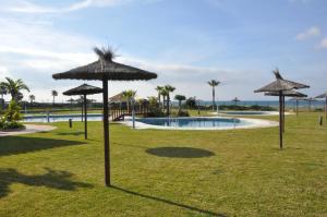 a pool with straw umbrellas in a park at Zahara almadraba playa Atlanterra in Zahara de los Atunes