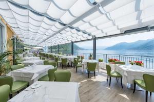 un restaurante con mesas y sillas blancas y vistas al agua en Villa Belvedere Como Lake Relais, en Argegno