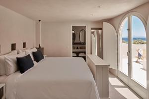 a white bedroom with a large bed and a balcony at Istoria, a Member of Design Hotels in Perivolos