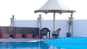 un grupo de sillas y una sombrilla junto a la piscina en Remas Hotel Suites - Al Khoudh, Seeb, Muscat, en Seeb
