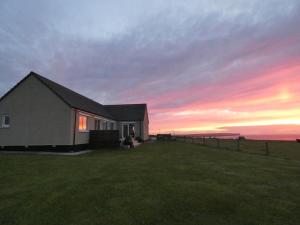 uma casa num campo com um pôr-do-sol ao fundo em Braeswick B&B em Sanday