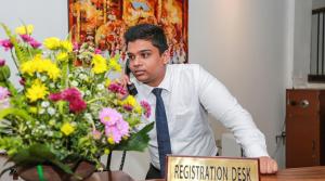 a man in a tie sitting at a table with flowers at Senani Hotel in Kandy
