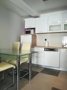 uma cozinha com armários brancos, uma mesa de vidro e cadeiras em Apartman Brzović em Omiš
