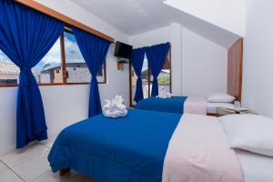 2 Betten in einem Zimmer mit blauen Vorhängen und einem Fenster in der Unterkunft Hostal Tongo Reef in Puerto Baquerizo Moreno