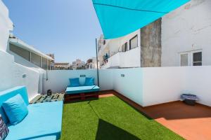 Faro Cosy Guesthouse في فارو: شرفة مع كراسي زرقاء وعشب على مبنى