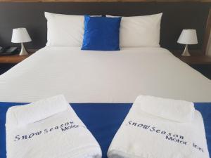 a bed with white sheets and blue pillows at Snow Season Motor Inn in Cooma