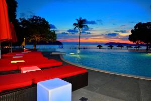 a resort pool with red chairs and umbrellas at sunset at Holiday Villa Resort & Beachclub Langkawi in Pantai Cenang