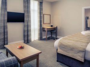 a room with a bed, chair, table and a television at Mercure Hatfield Oak Hotel in Hatfield