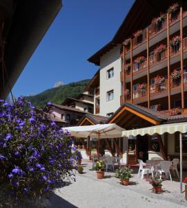 a hotel with tables and chairs and purple flowers at Hotel Zurigo in Molveno