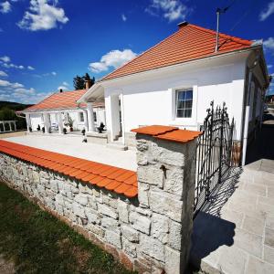 a white house with an orange roof and a stone wall at Vidéki Varázs Vendégház in Bogács