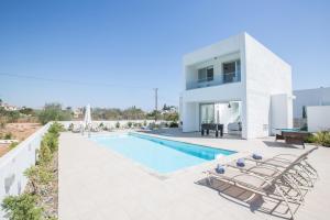 eine weiße Villa mit einem Pool und Stühlen in der Unterkunft Greco Villas in Protaras