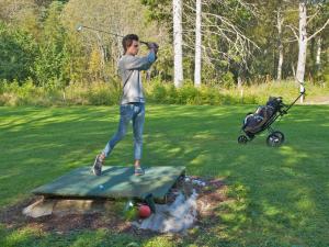 Um homem a balançar um taco de golfe numa mesa com um carrinho de bebé. em Kårstua - Austrått Agroturisme em Austrått